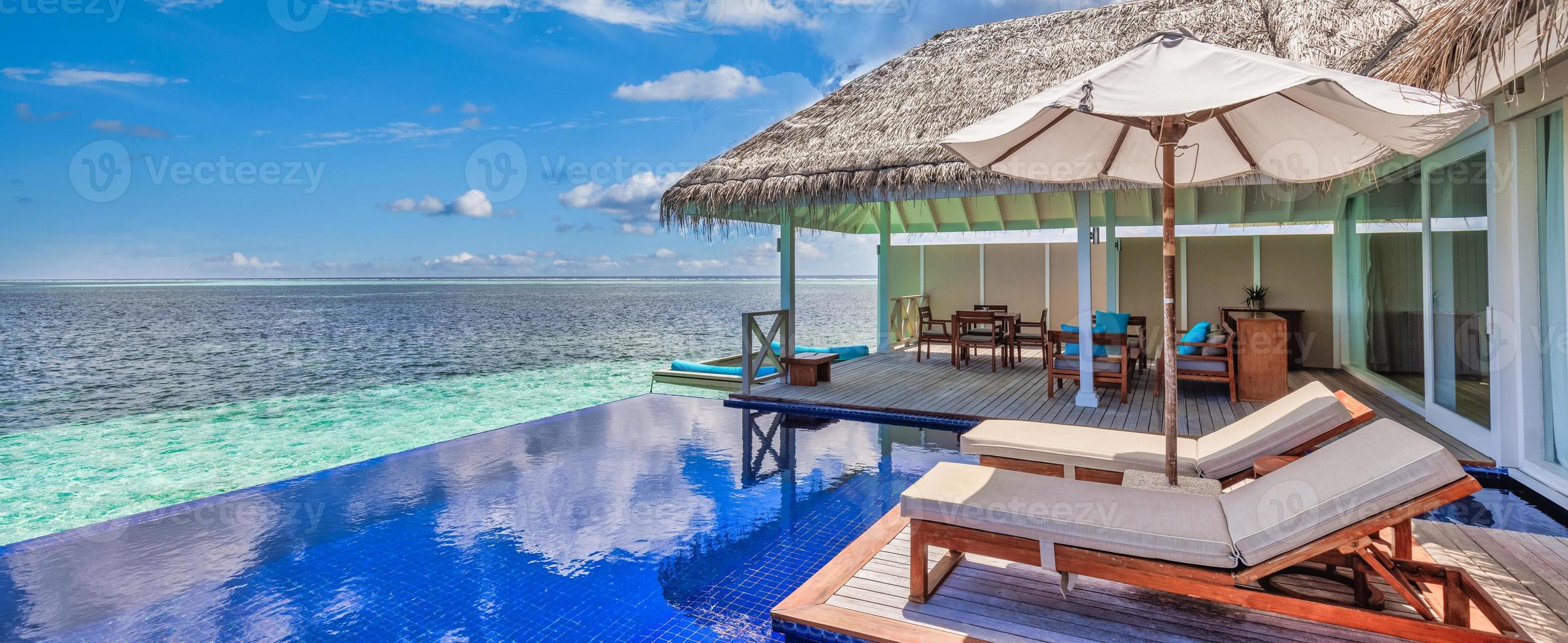 hermoso paisaje marino de viaje panorámico, lujosas vacaciones románticas en la playa para parejas de luna de miel, vacaciones tropicales en un lujoso complejo hotelero. increíble villa de agua con sillas y sombrilla, piscina infinita foto