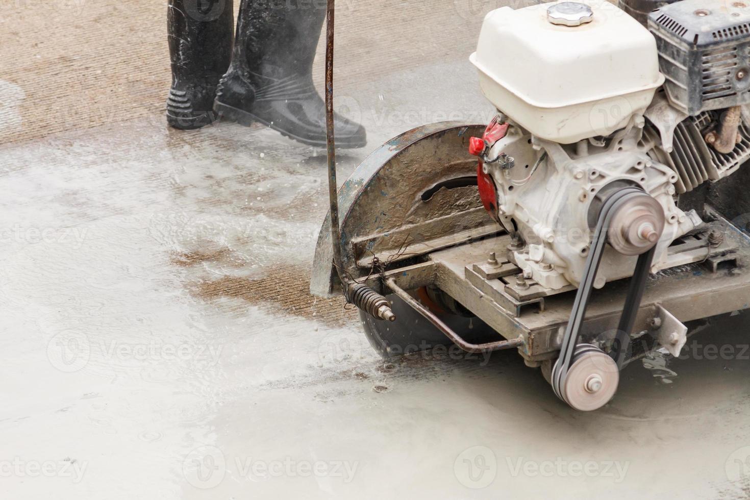 Worker using diamond saw blade machine cutting concrete road at construction site photo