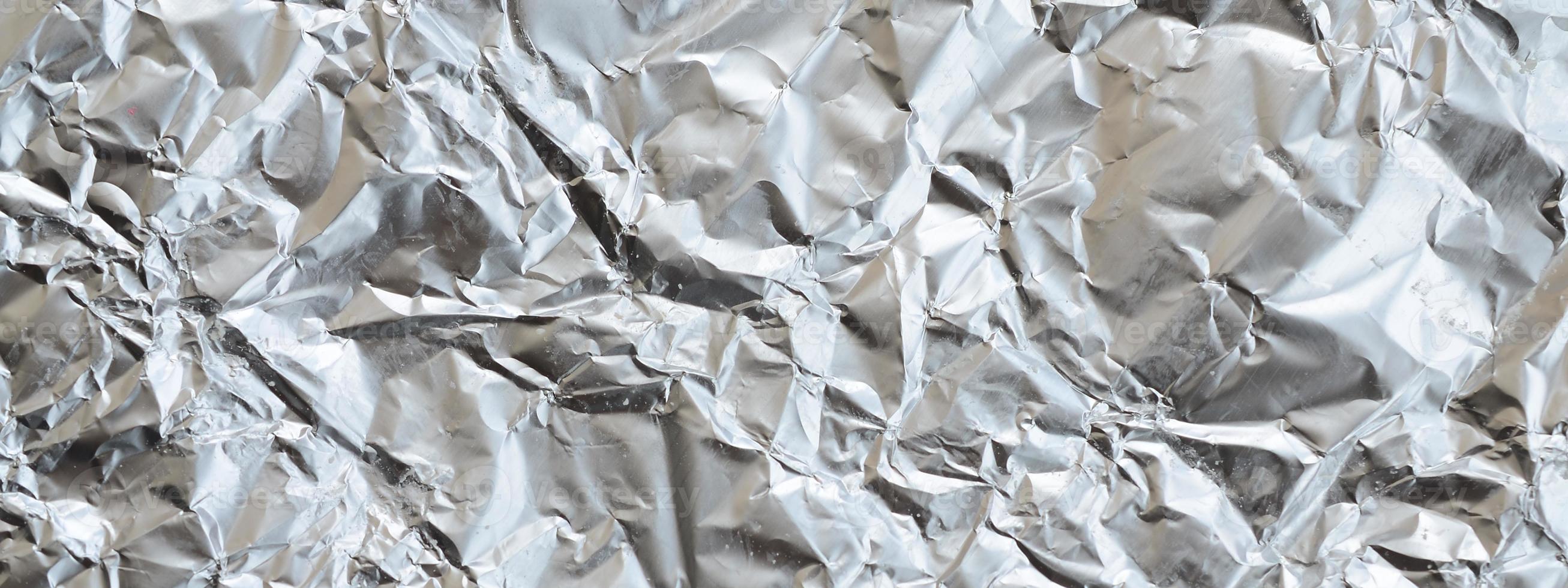 Thin wrinkled sheet of crushed tin aluminum silver foil background with shiny crumpled surface for texture photo