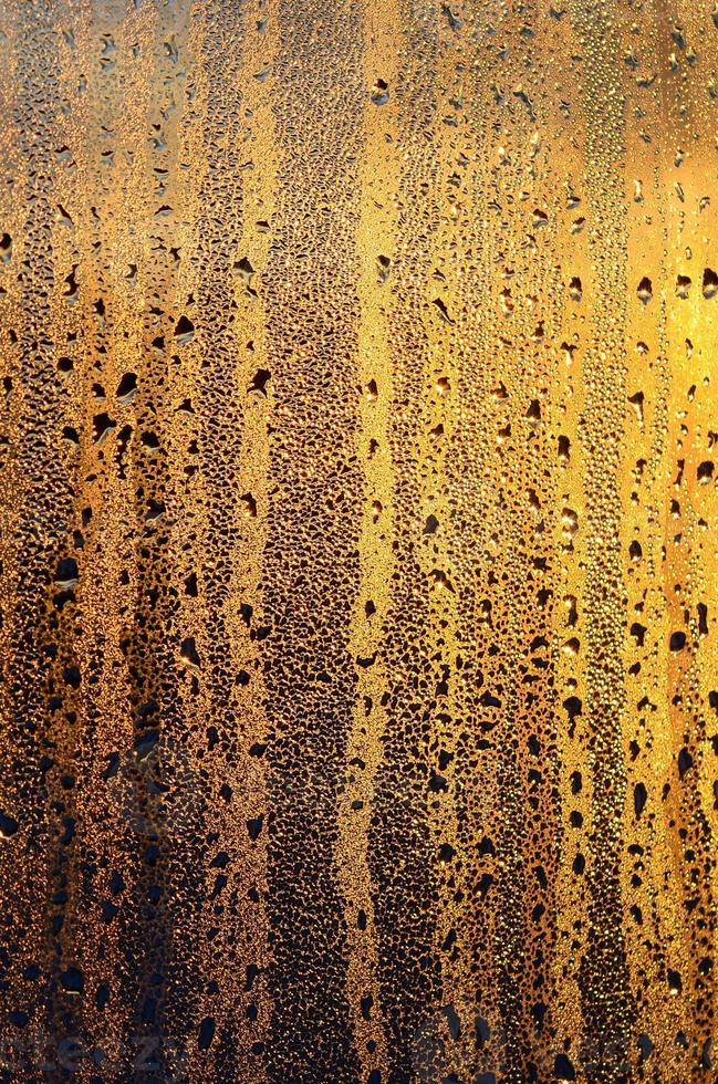 The texture of misted glass with a lot of drops and drips of condensation against the sunlight at dawn. Background image photo