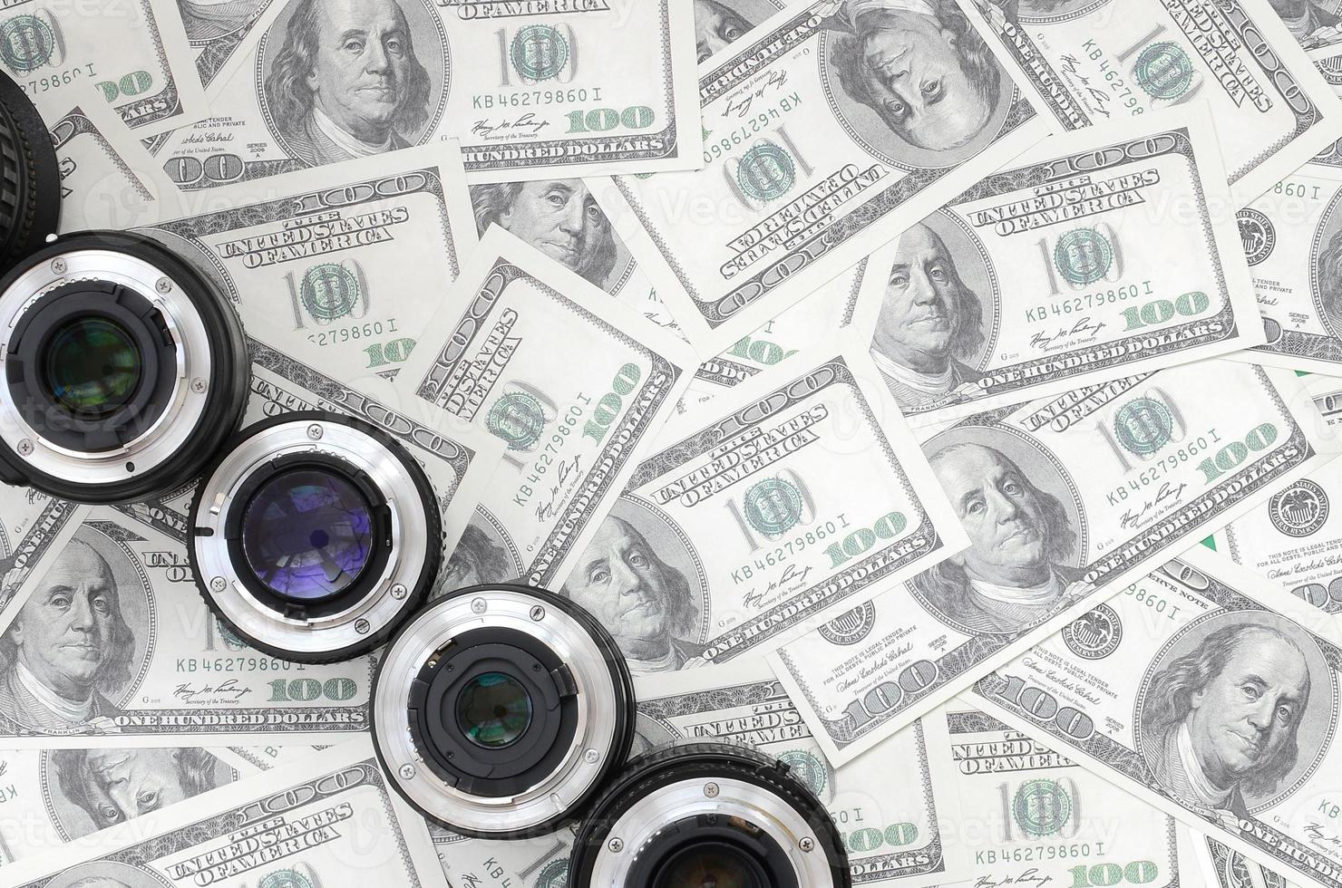 A few photographic lenses lies on the background of a lot of dollar bills. Space for text photo