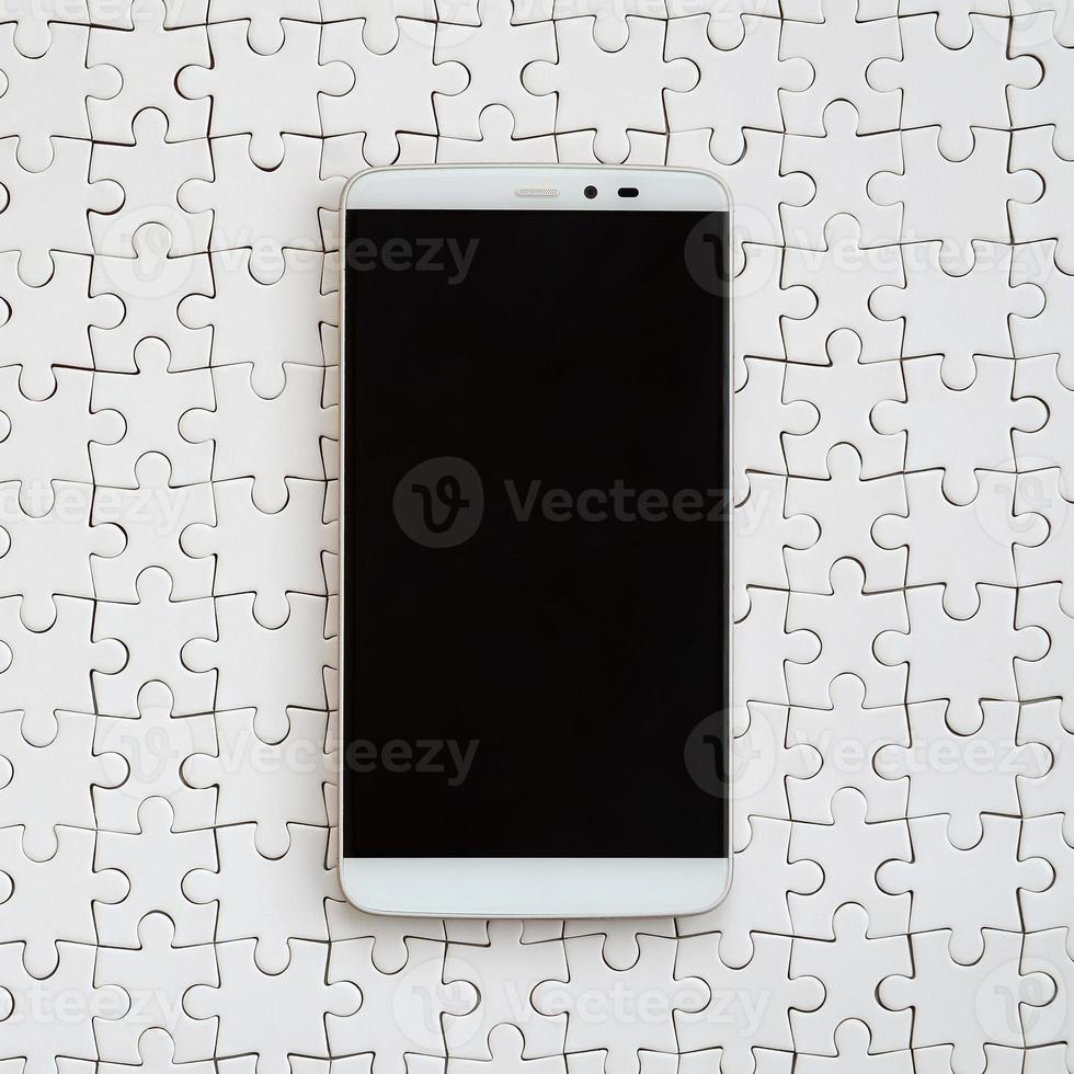 A modern big smartphone with a touch screen lies on a white jigsaw puzzle in an assembled state photo