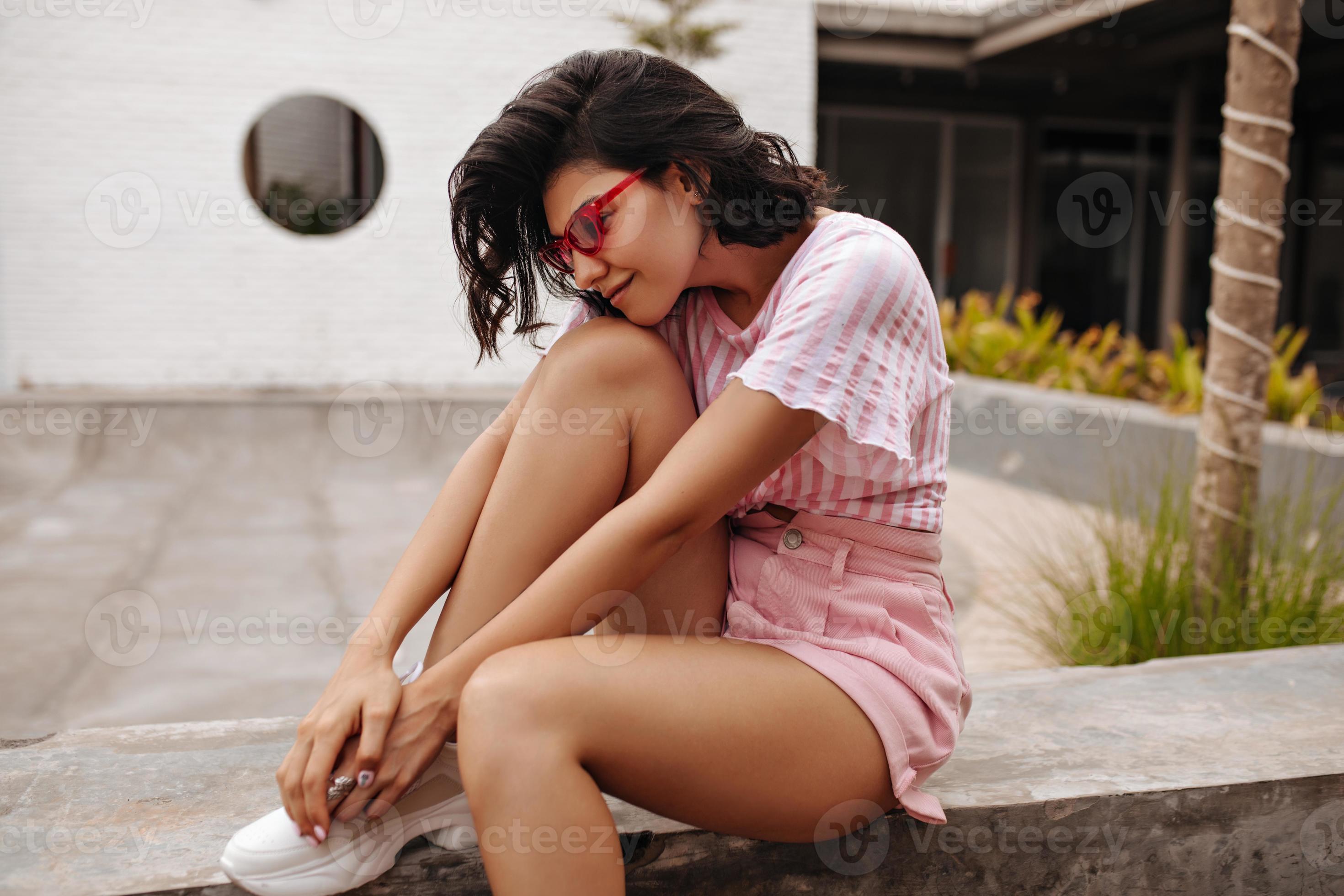 Goodlooking girl in shorts sitting on urban background. Outdoor shot
