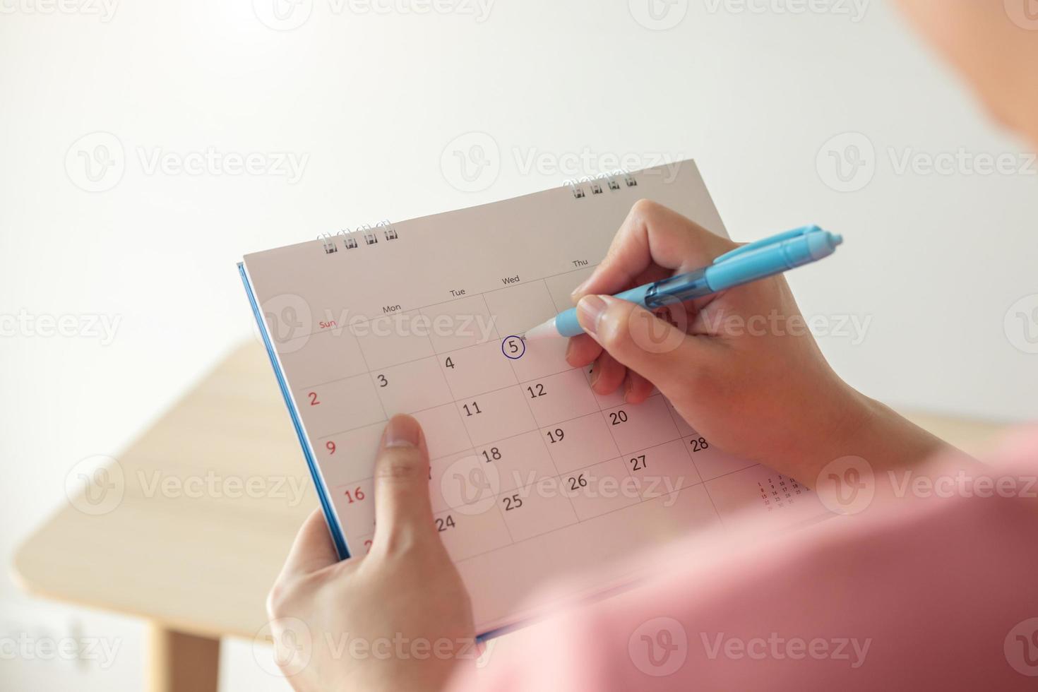 Hand with pen mark at 5th on calendar date with blue circle photo