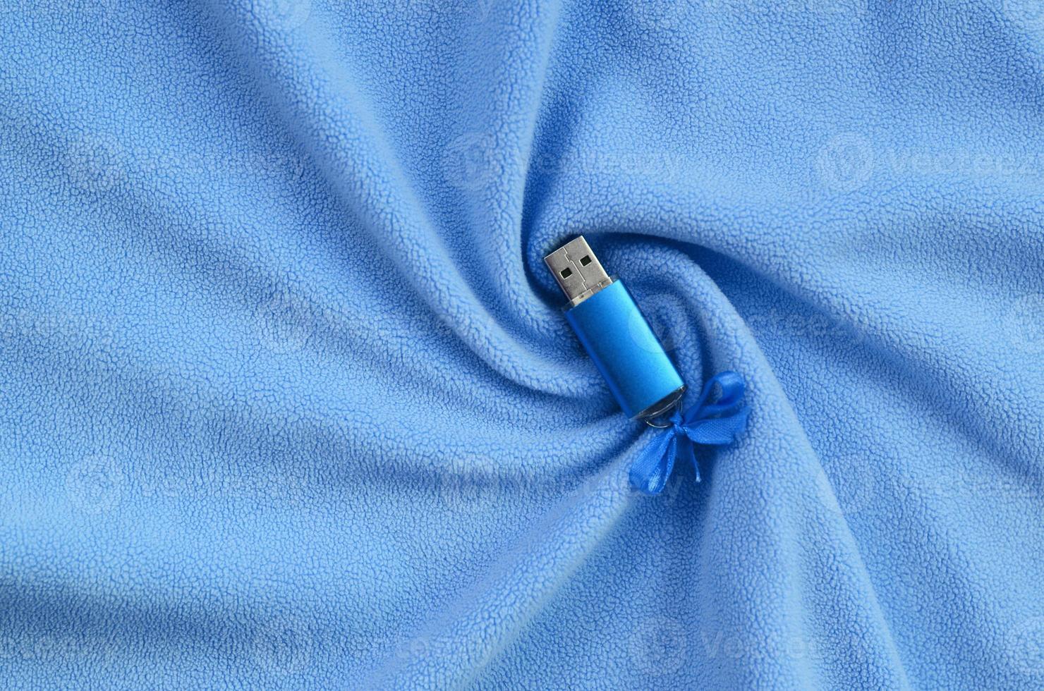 Brilliant blue usb flash memory card with a blue bow lies on a blanket of soft and furry light blue fleece fabric with a lot of relief folds. Memory storage device in women's design photo