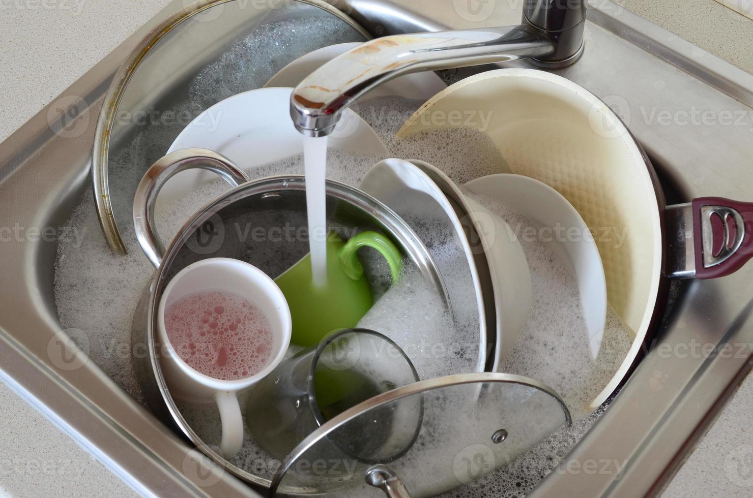 platos sucios y electrodomésticos de cocina sin lavar yacen en agua de espuma bajo un grifo de cocina foto