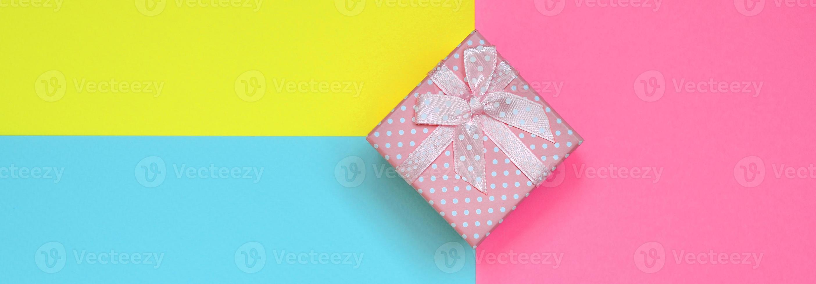 Small pink gift box lie on texture background of fashion pastel blue, yellow and pink colors paper in minimal concept photo