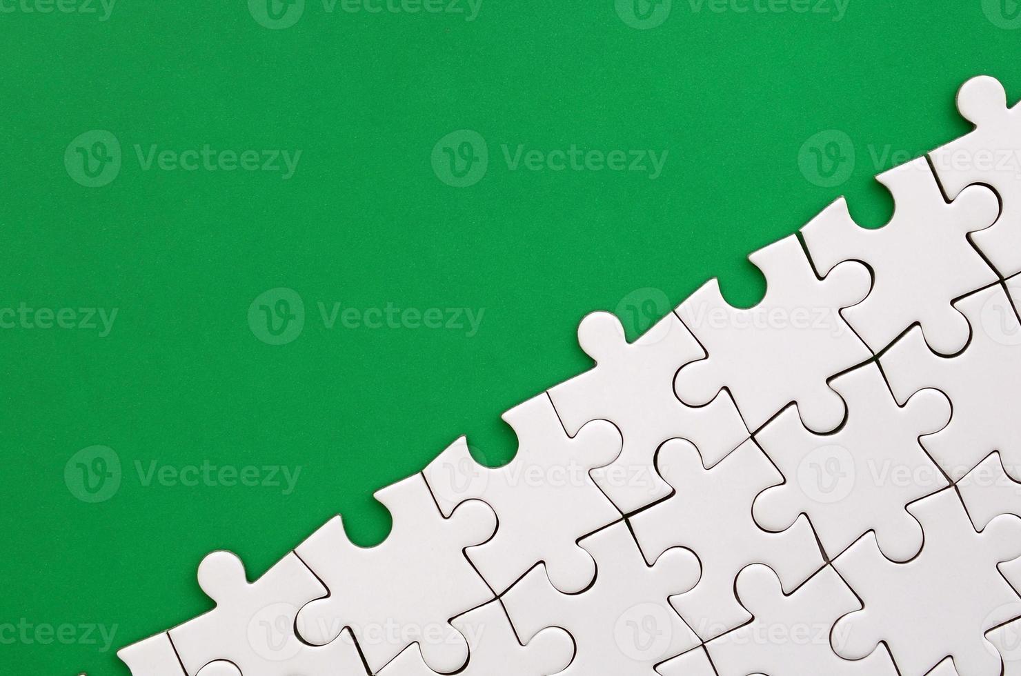 Fragment of a folded white jigsaw puzzle on the background of a green plastic surface. Texture photo with copy space for text