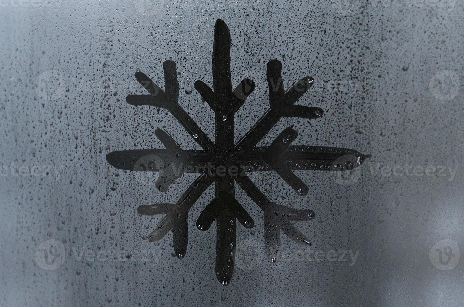 The image of the snowflake is drawn with a finger on the surface of a misted glass window. Frosty weather photo