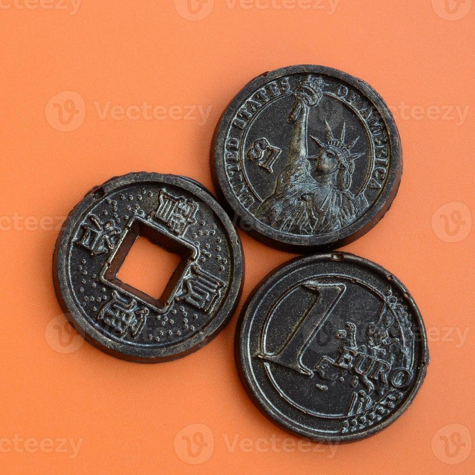 Three chocolate products in the form of Euro, USA and Japan coins lie on an orange plastic background. A model of cash coins in an edible form photo