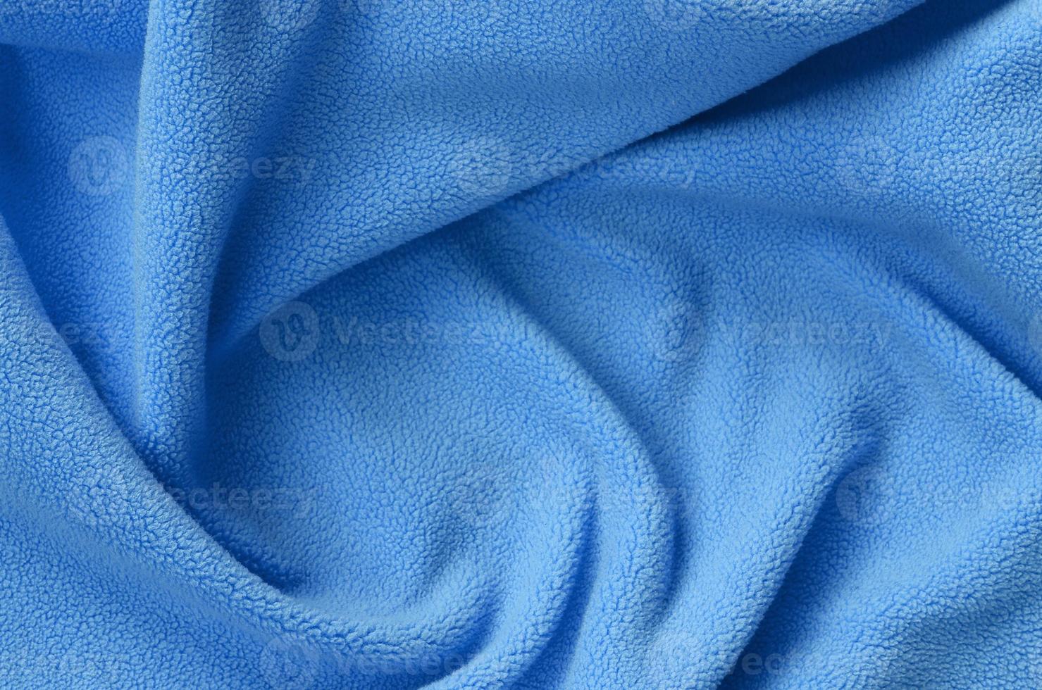 The blanket of furry blue fleece fabric. A background of light blue soft plush fleece material with a lot of relief folds photo