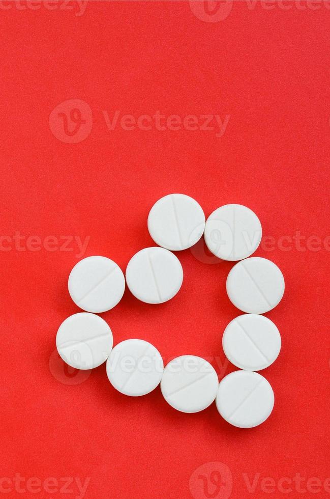 Several white tablets lie on a bright red background in the shape of a heart. Background image on medicine and pharmaceutical topics photo