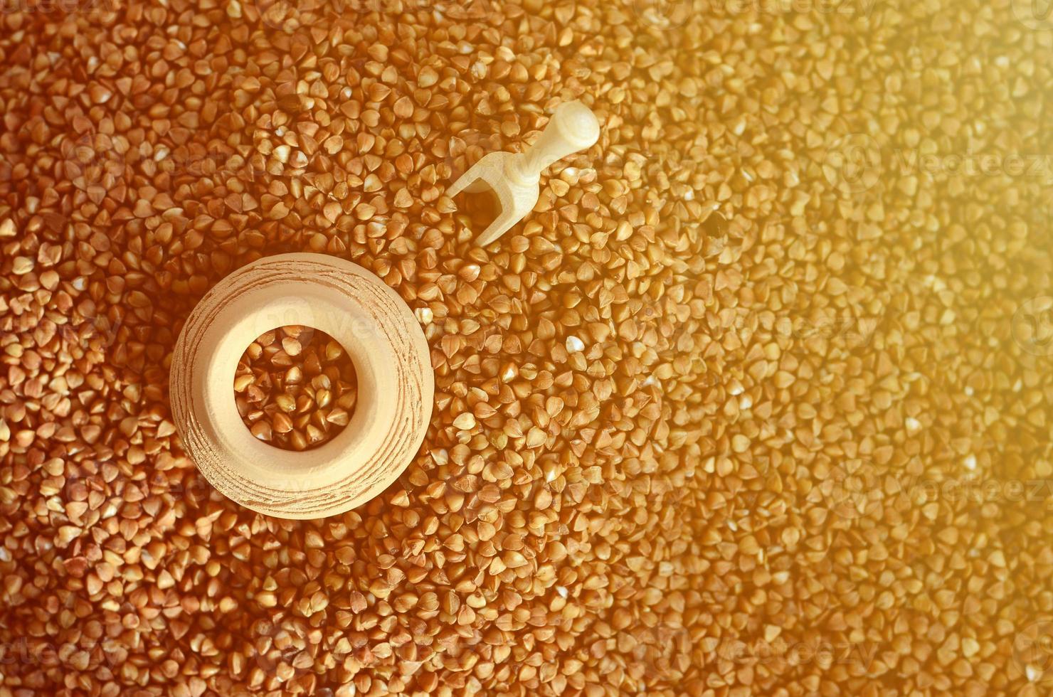 Background image of a large pile of buckwheat, in the middle of which lies a small jug and a wooden spatula for cereals photo