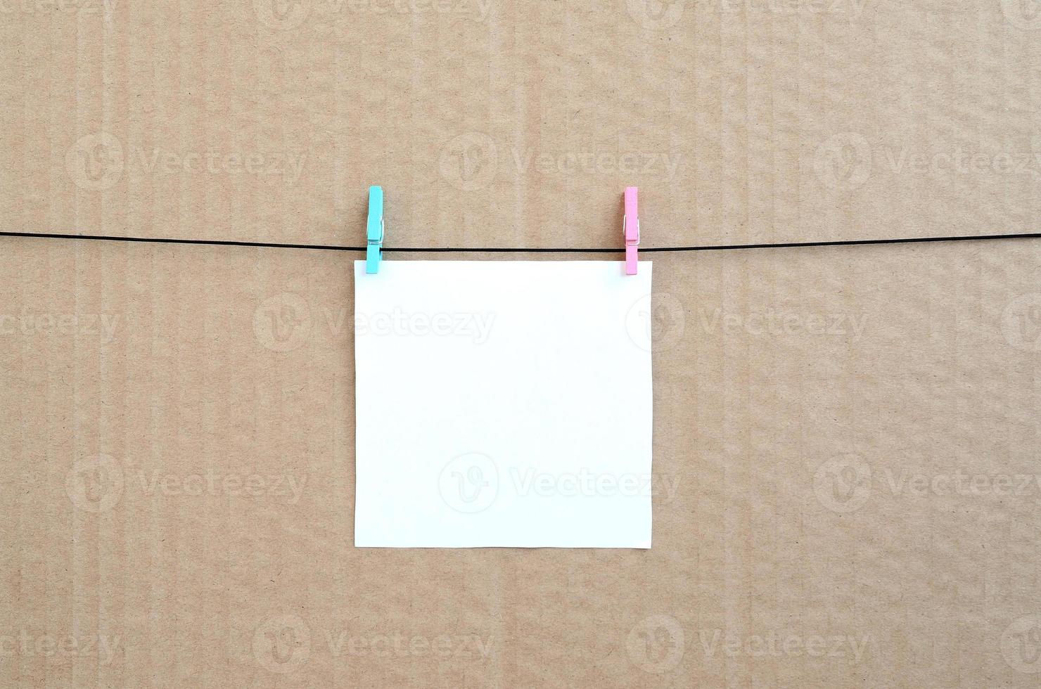 White blank card on rope on a brown cardboard background. Creative reminder, small sheet of paper on wooden clothespin, memo backdrop photo