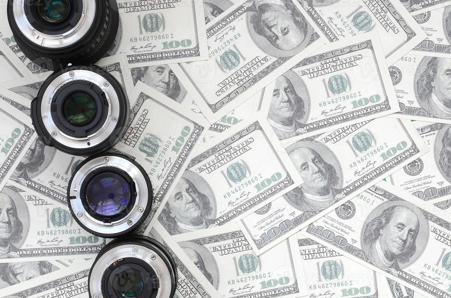 A few photographic lenses lies on the background of a lot of dollar bills. Space for text photo