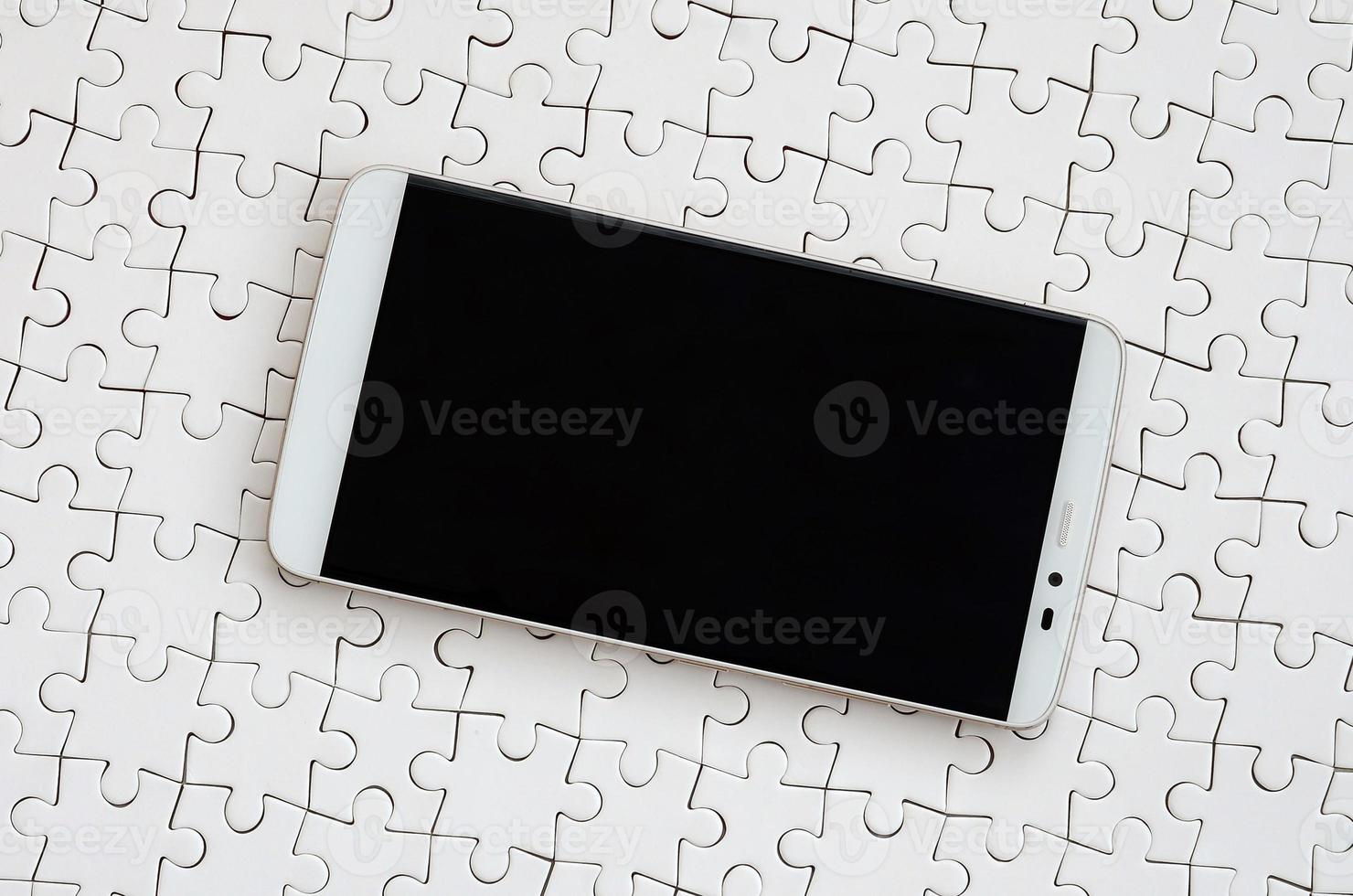 A modern big smartphone with a touch screen lies on a white jigsaw puzzle in an assembled state photo