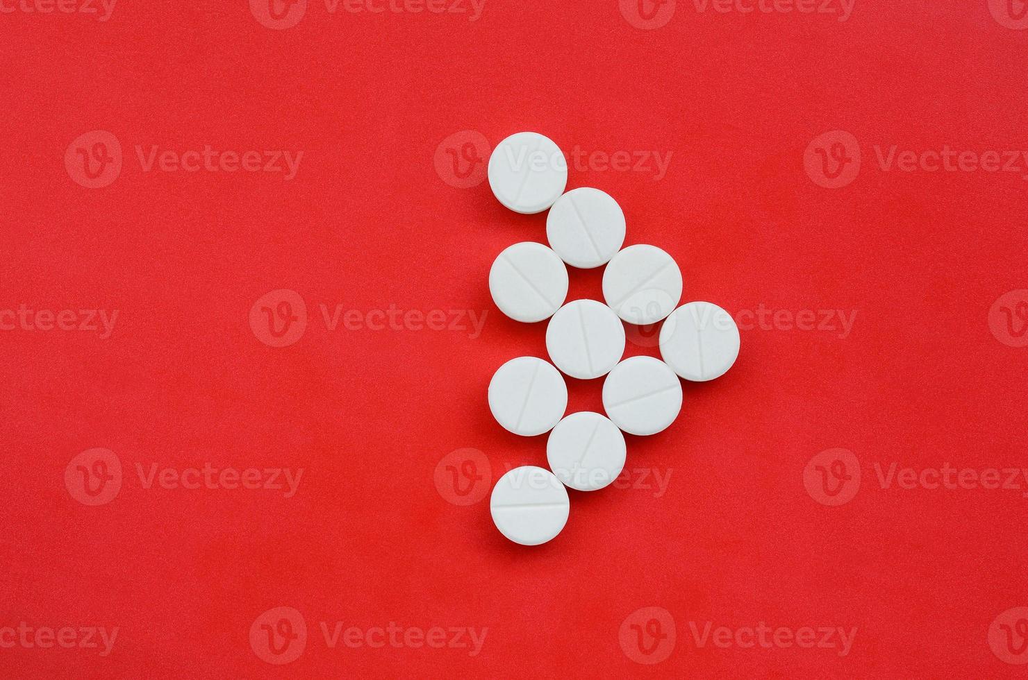 Several white tablets lie on a bright red background in the form of a triangular arrow. Background image on medicine and pharmaceutical topics photo