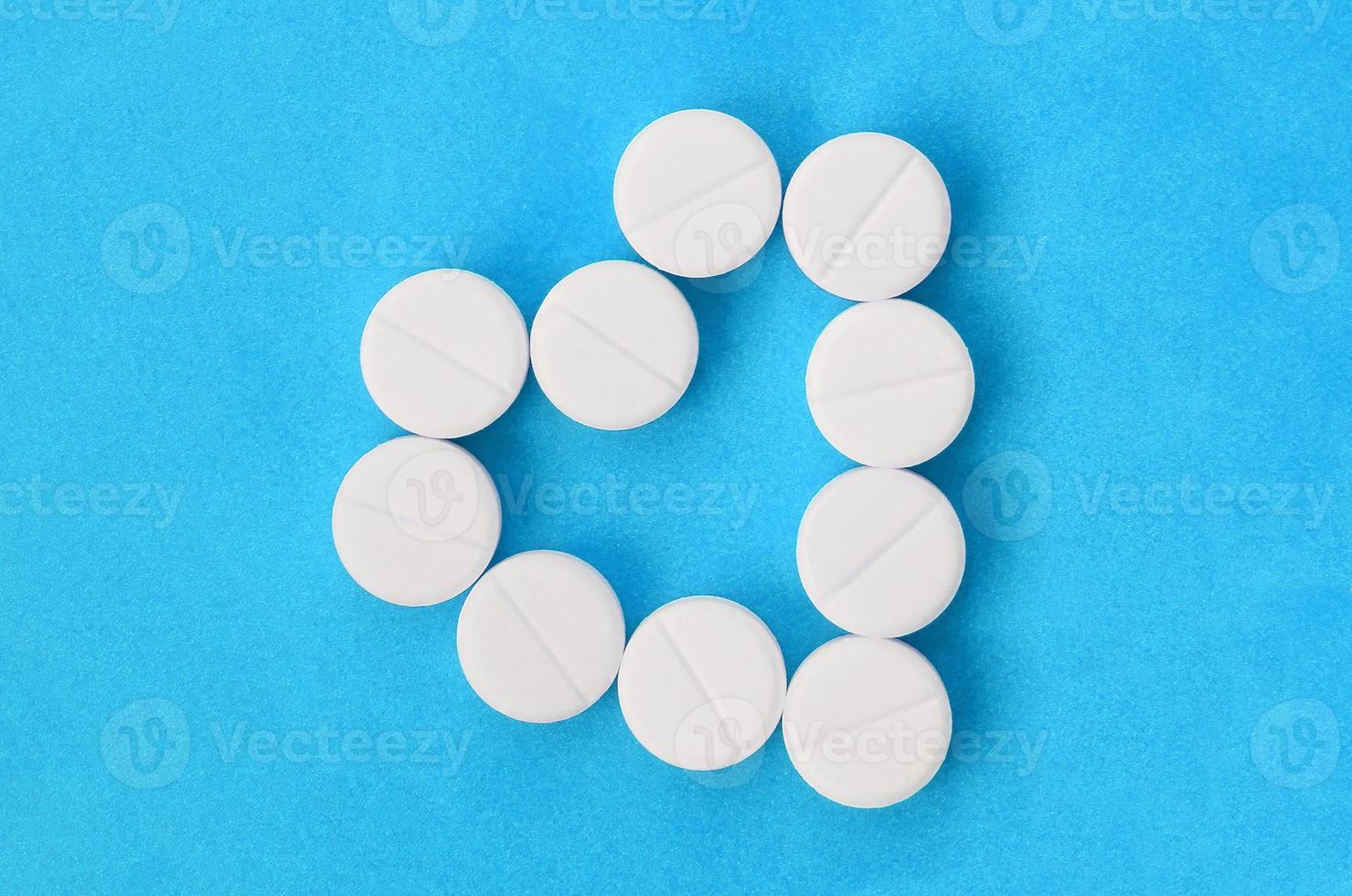 Several white tablets lie on a bright blue background in the shape of a heart. Background image on medicine and pharmaceutical topics photo