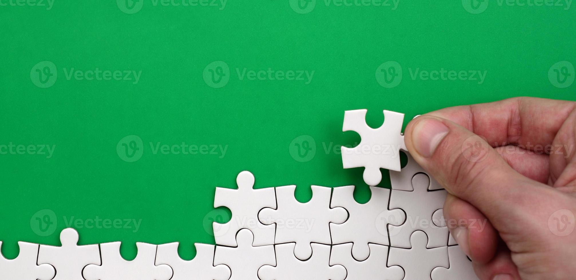 The hand folds a white jigsaw puzzle against the background of the green surface. Texture photo with space for text