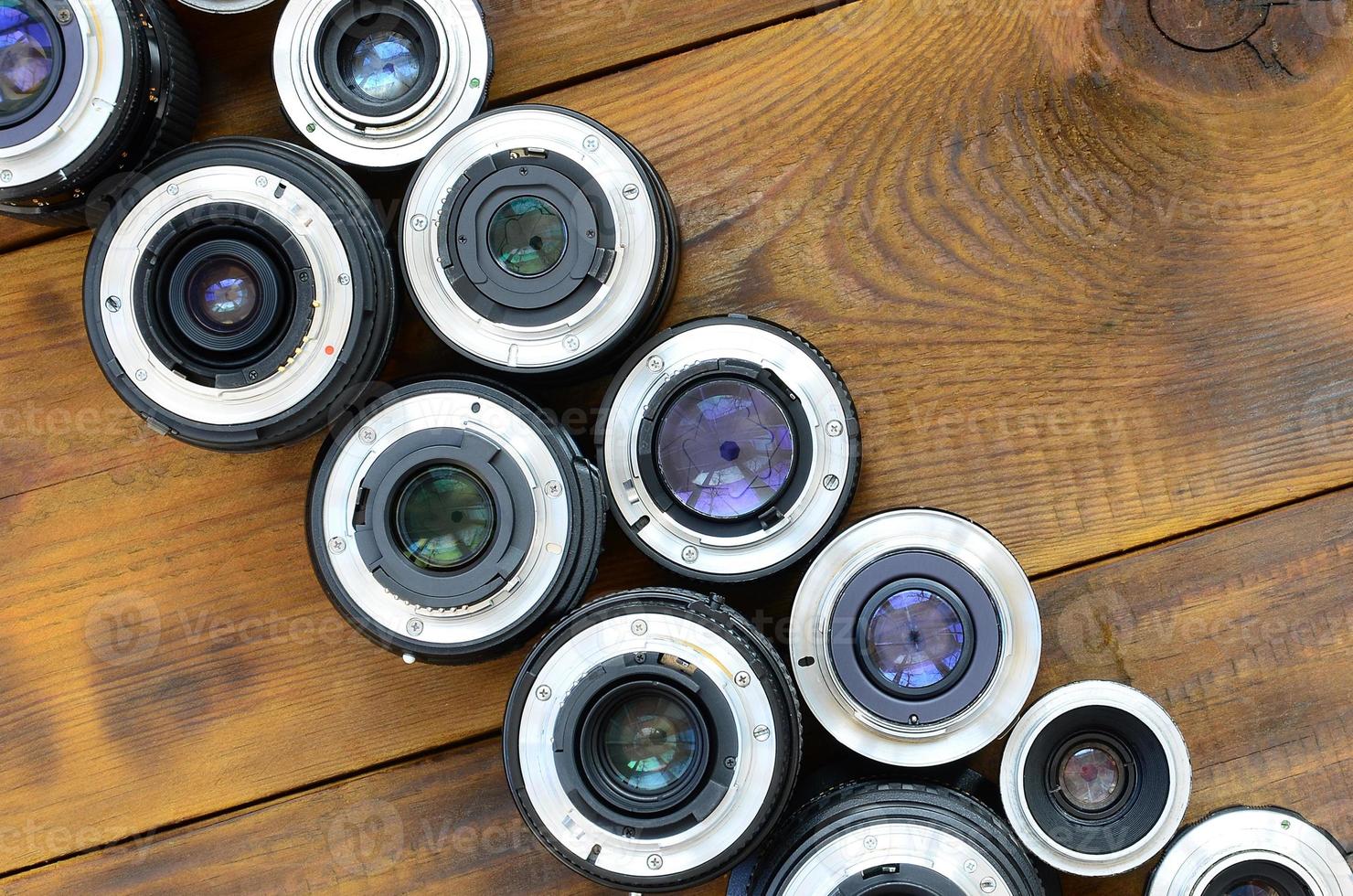 Several photographic lenses lie on a brown wooden background. Space for text photo