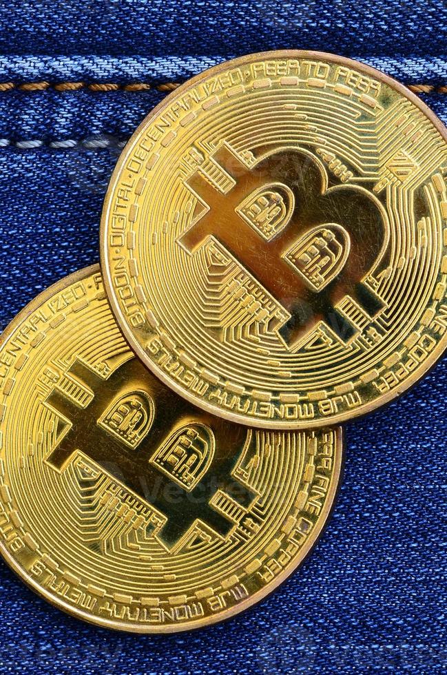 Two golden Bitcoins is lies on a blue jeans fabric. New virtual money. New crypto currency in the form of the coins photo