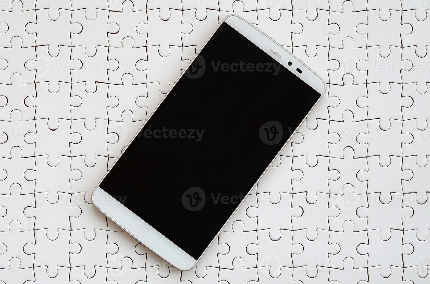 A modern big smartphone with a touch screen lies on a white jigsaw puzzle in an assembled state photo