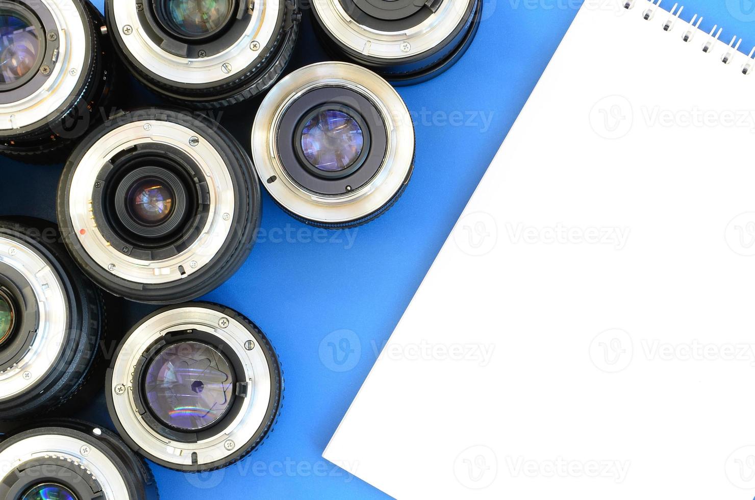 Several photographic lenses and white notebook lie on a bright blue background. Space for text photo