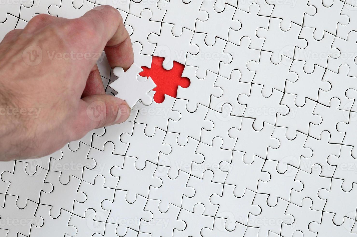 The texture of a white puzzle puzzle in the assembled state with one missing element that the male hand puts in photo