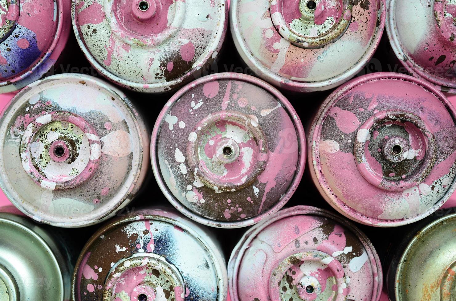 unas pocas latas de aerosol usadas con gotas de pintura rosa se encuentran en el fondo de textura de papel de color rosa pastel de moda en un concepto mínimo foto