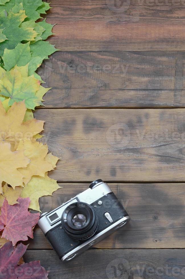 The old camera among a set of yellowing fallen autumn leaves on a background surface of natural wooden boards of dark brown color photo