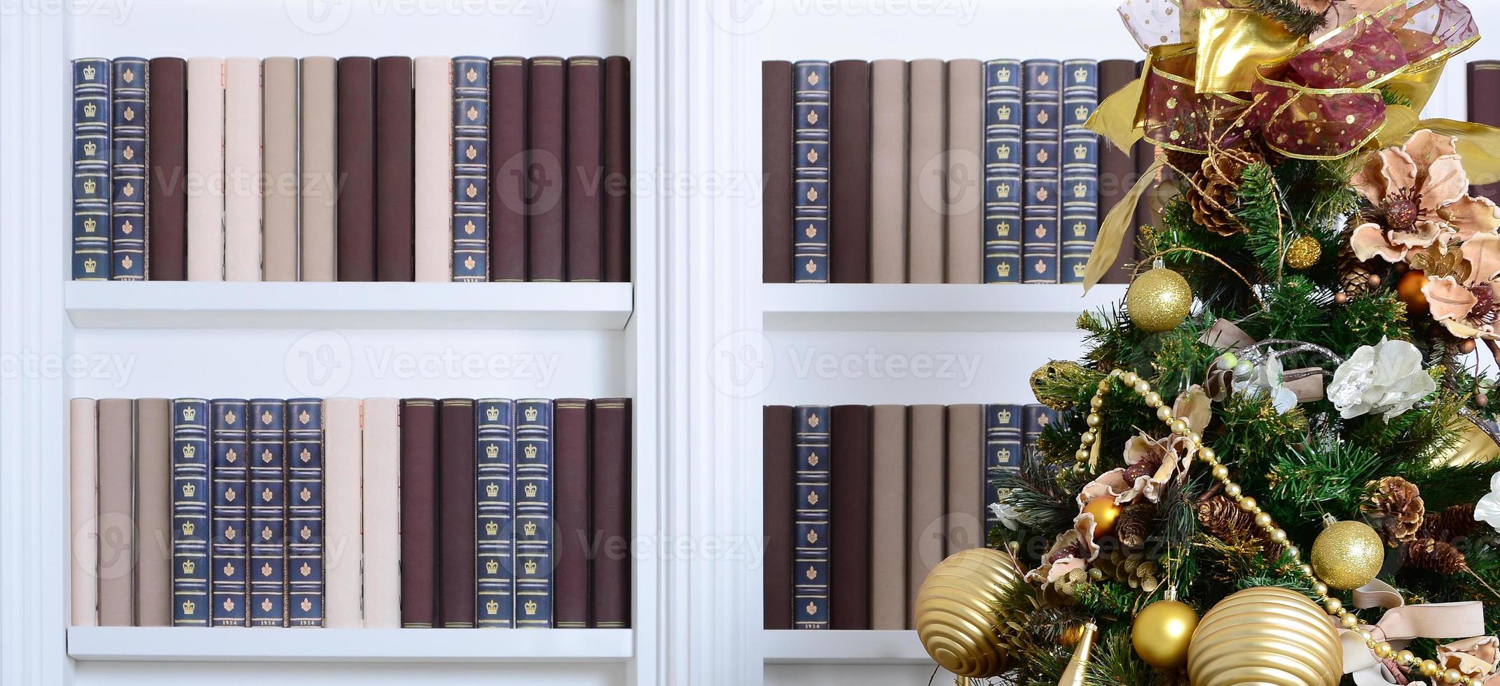 A beautiful decorated Christmas tree on the background of a bookshelf with many books of different colors. Christmas background image of the library photo