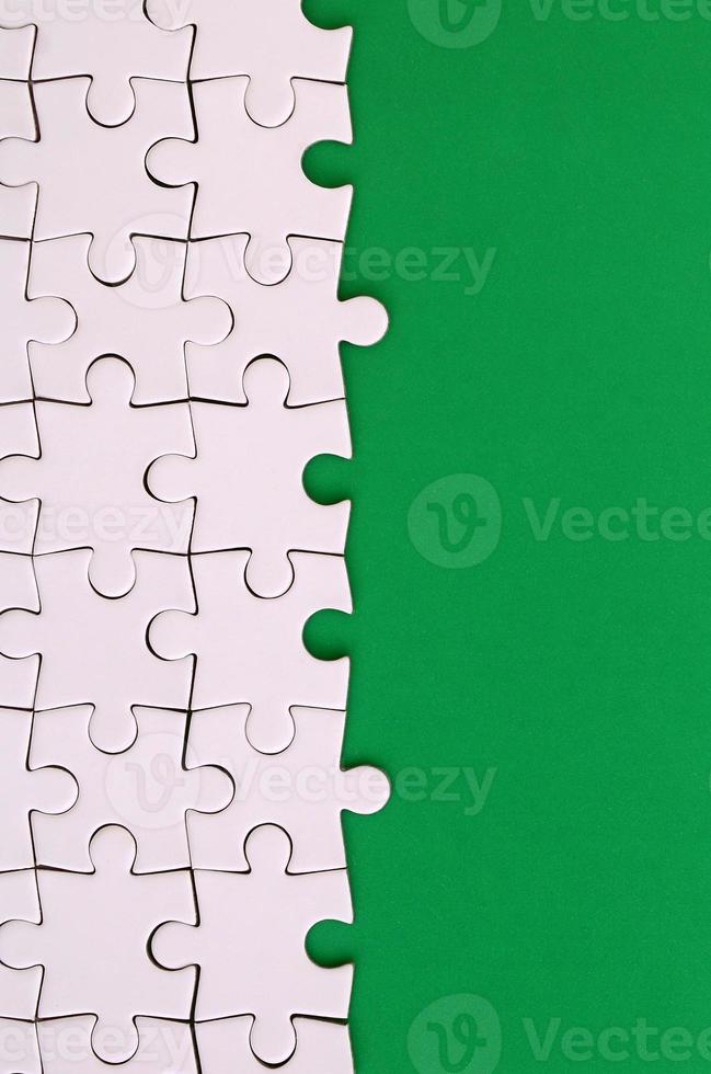 Fragment of a folded white jigsaw puzzle on the background of a green plastic surface. Texture photo with copy space for text