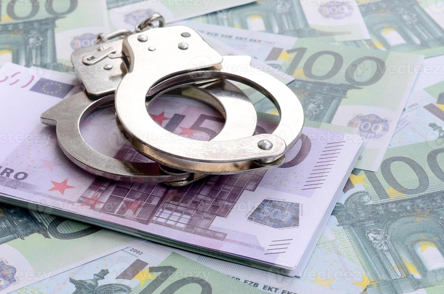 Police handcuffs lies on a set of green monetary denominations of 100 euros. A lot of money forms an infinite heap photo