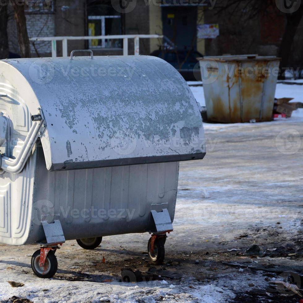 A silver garbage container stands near residential buildings in winter photo