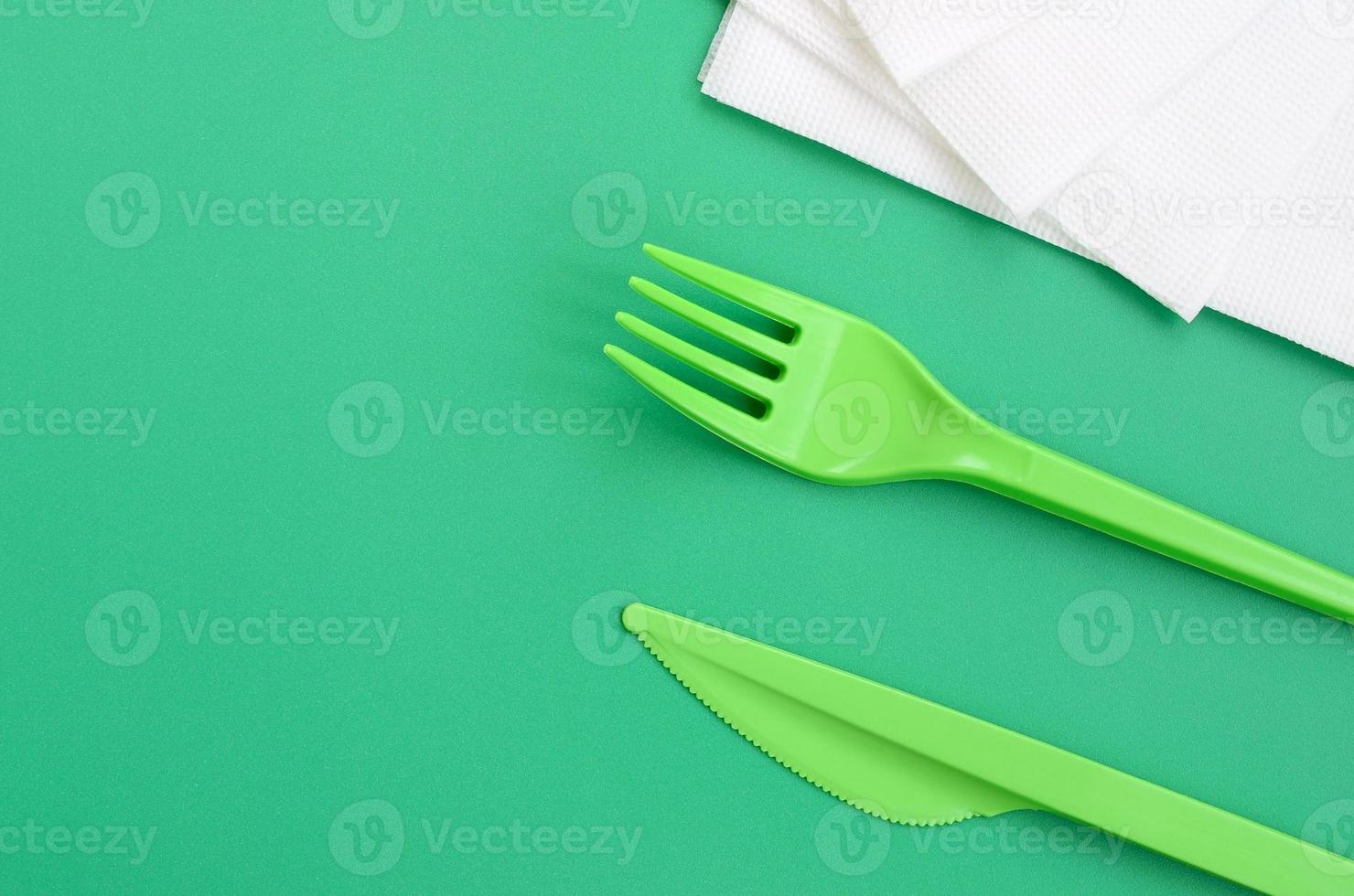 Disposable plastic cutlery green. Plastic fork and knife lie on a green background surface next to napkins photo