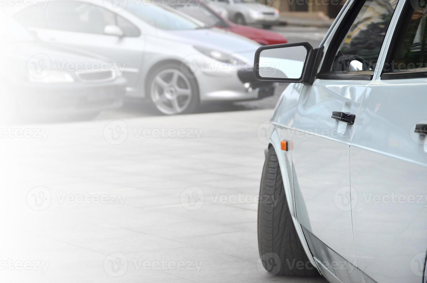 Diagonal view of a white glossy car that stands on a square of gray tiles photo