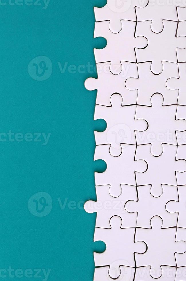 Fragment of a folded white jigsaw puzzle on the background of a blue plastic surface. Texture photo with copy space for text