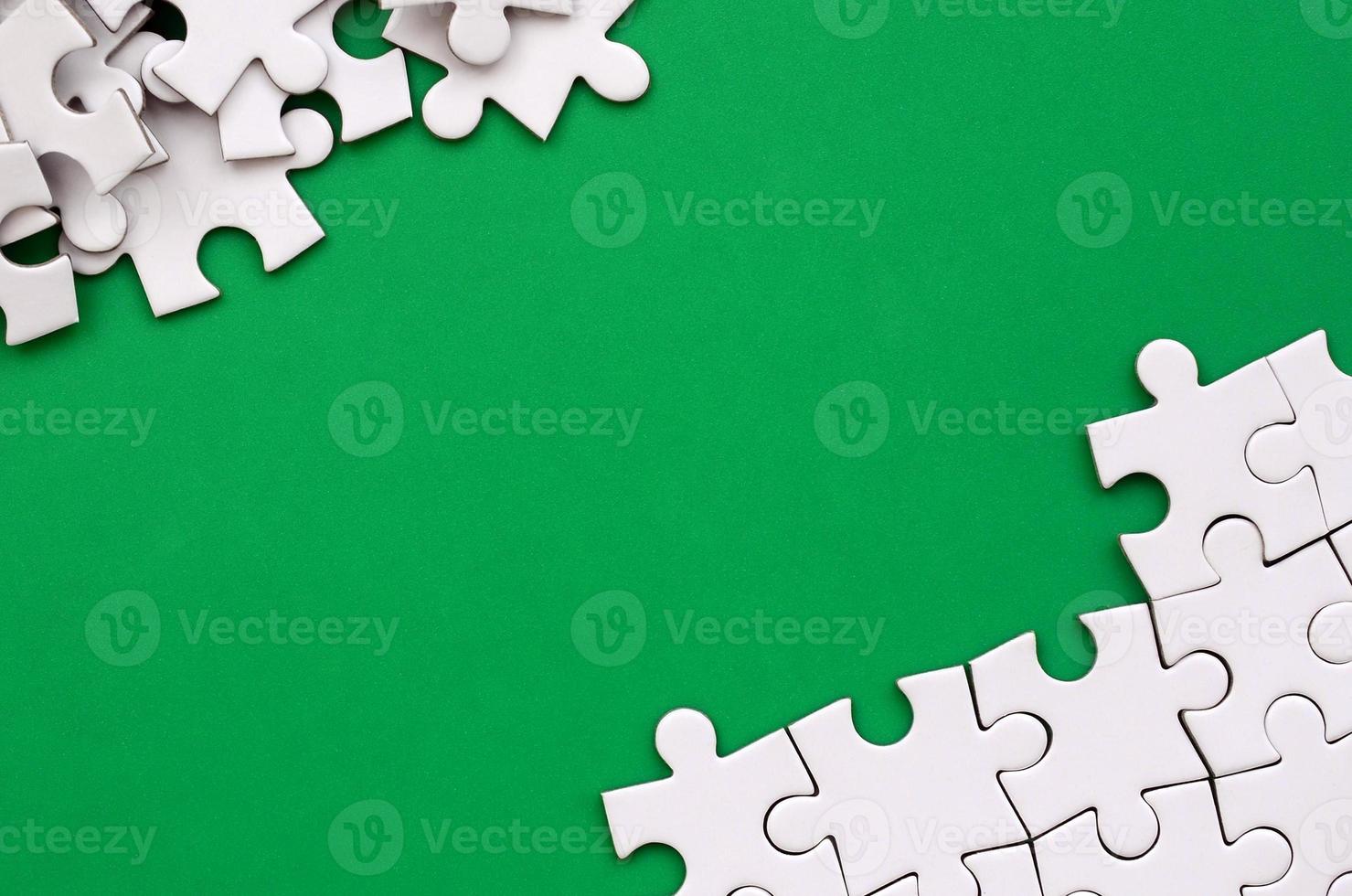 Fragment of a folded white jigsaw puzzle and a pile of uncombed puzzle elements against the background of a green surface. Texture photo with space for text