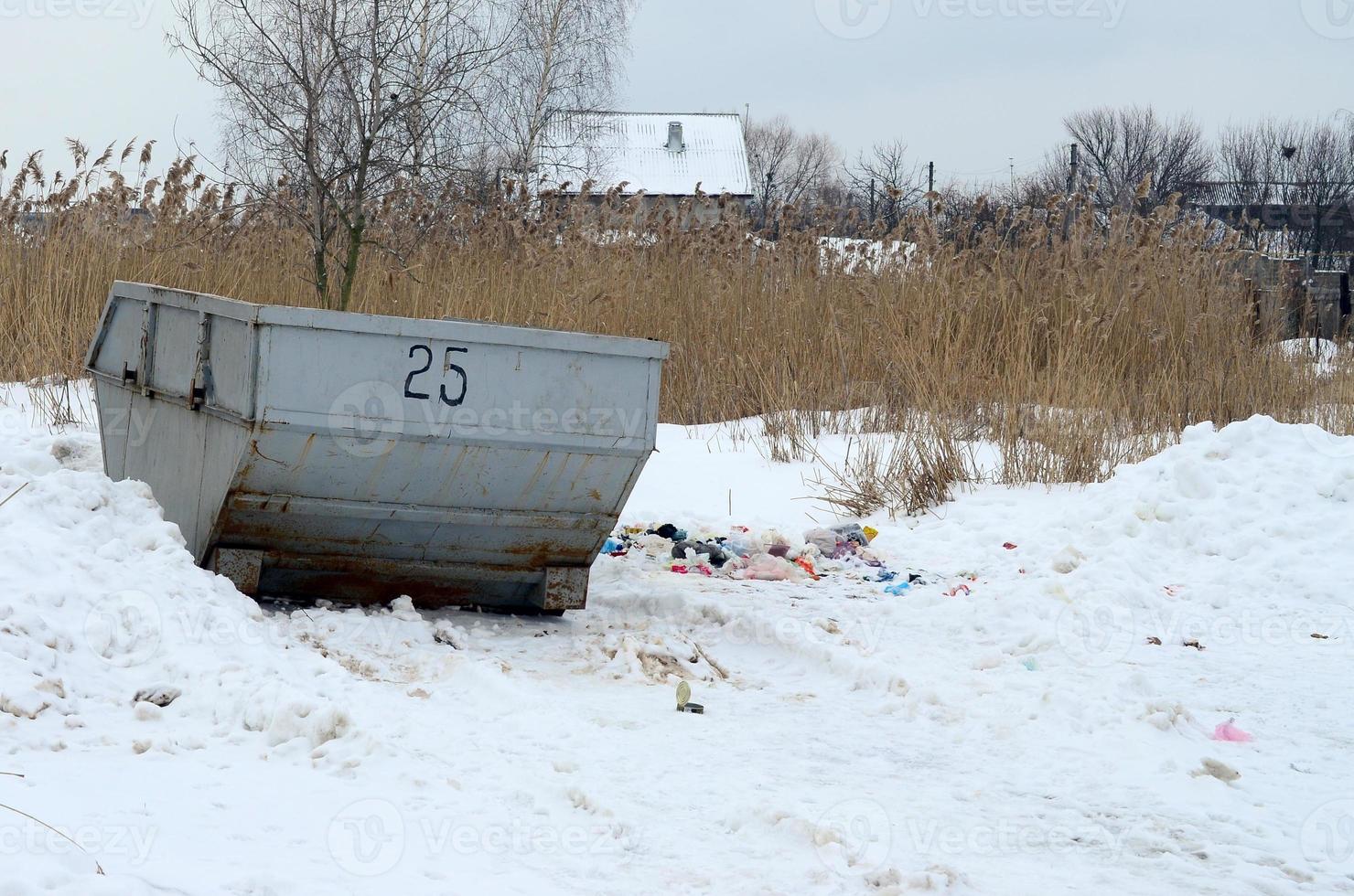 Trash bin at the side of street in winter with lip garbage container winter snow. Metal container for household waste photo