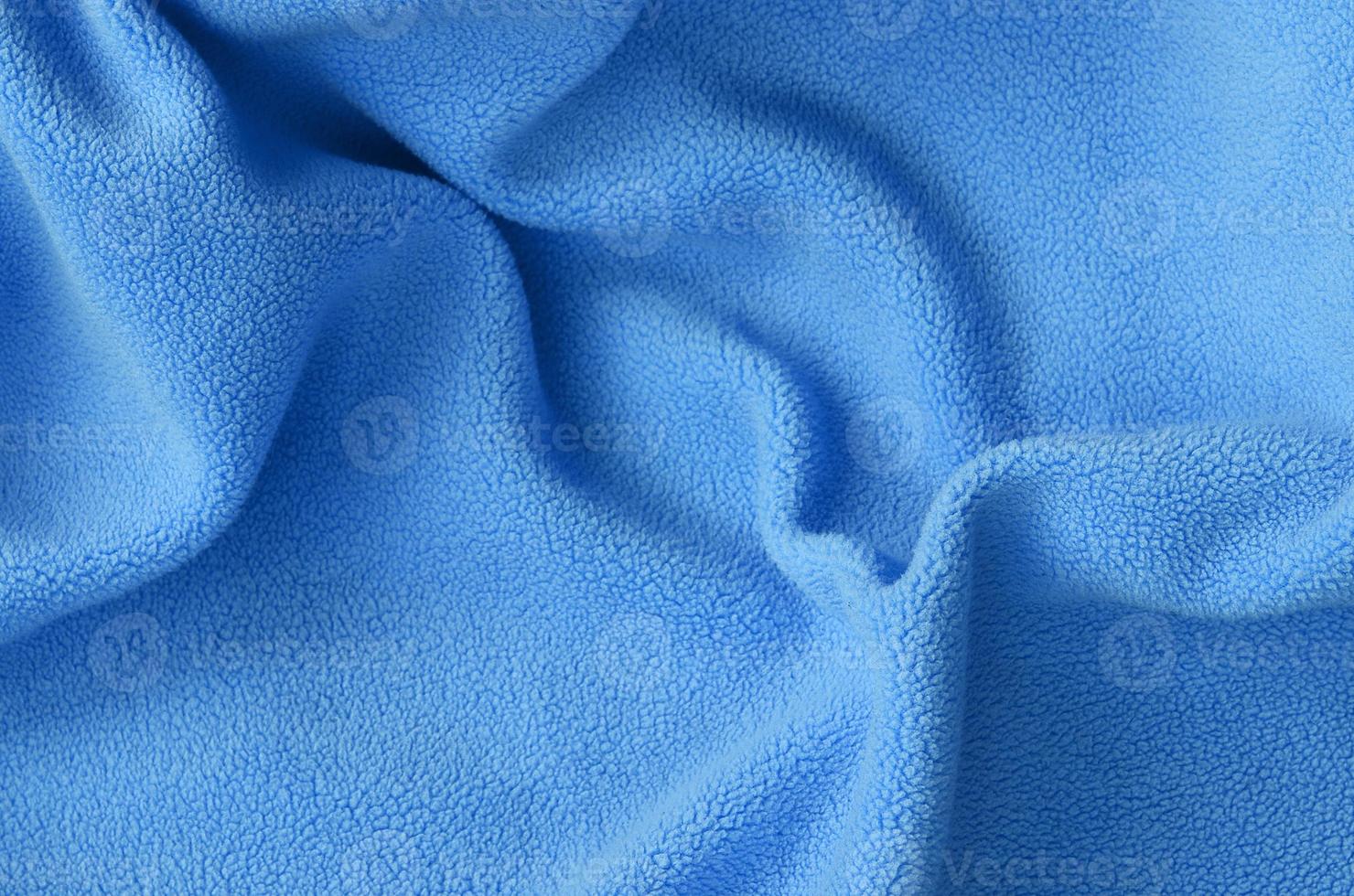 The blanket of furry blue fleece fabric. A background of light blue soft plush fleece material with a lot of relief folds photo