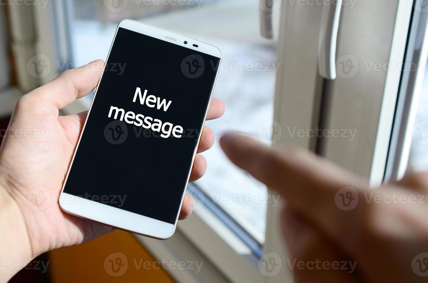 A person sees a white inscription on a black smartphone display that holds in his hand. New message photo