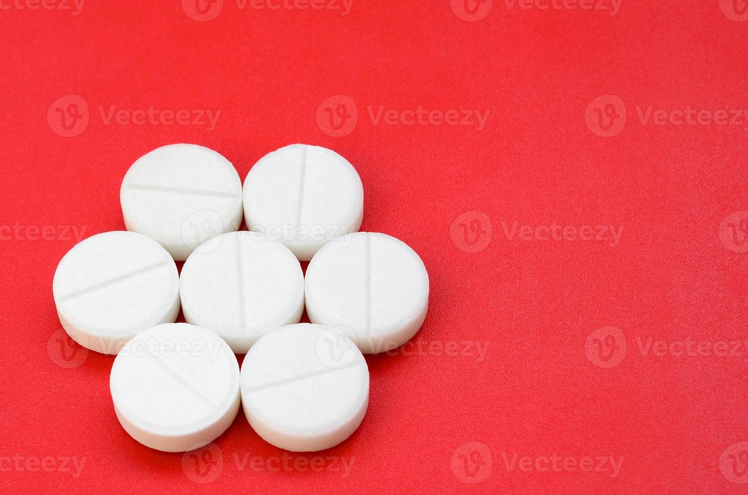 A few white tablets lie on a bright red background surface. Background image on medical and pharmaceutical topics photo