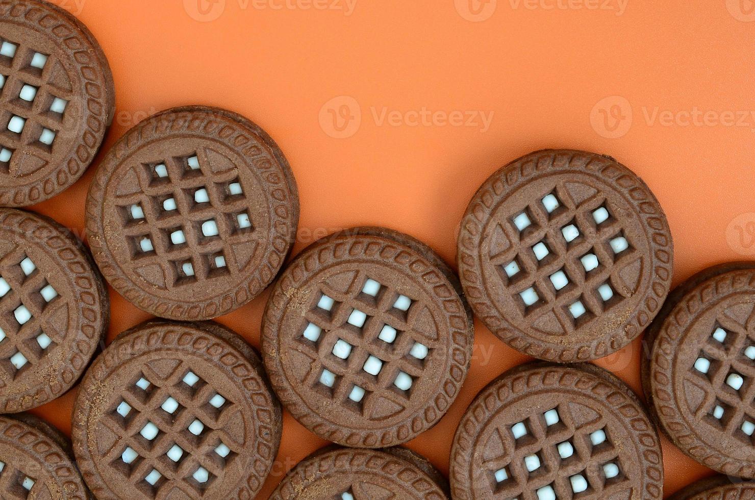 Detailed picture of dark brown round sandwich cookies with coconut filling on an orange surface. Background image of a close-up of several treats for tea photo