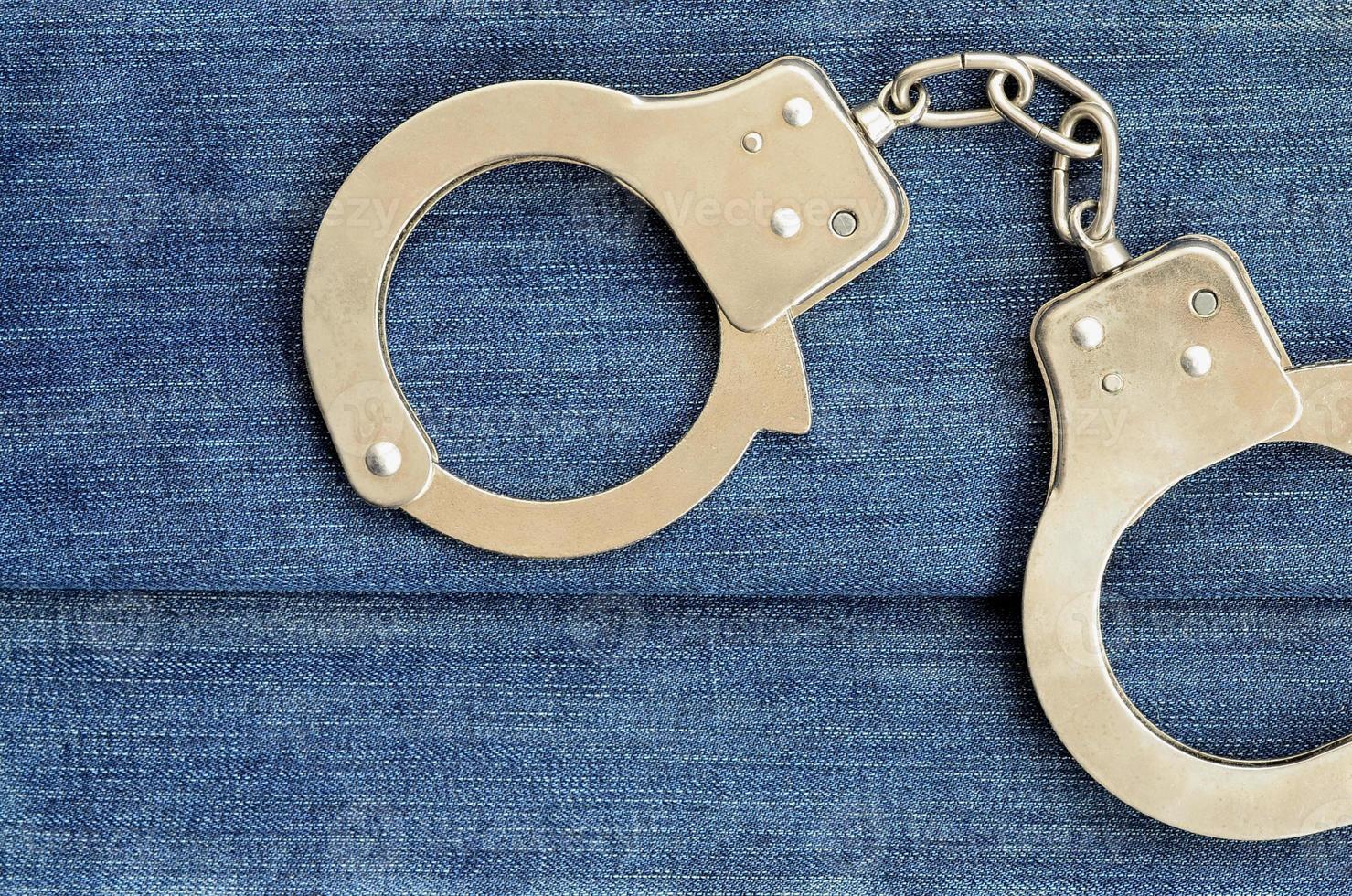 Police steel handcuffs lying on dark blue jeans background photo