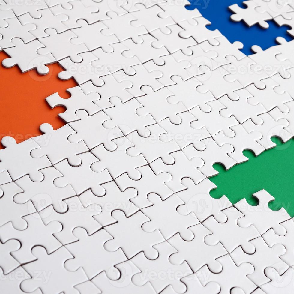 Close-up texture of a white jigsaw puzzle in assembled condition with missing elements, under which surfaces of different colors photo