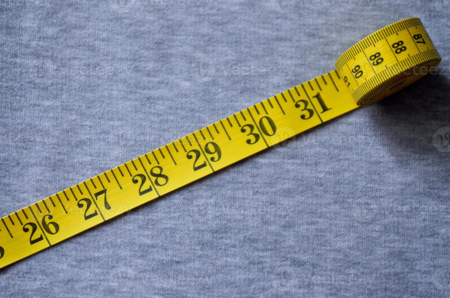 Yellow measuring tape lies on a gray knitted fabric photo