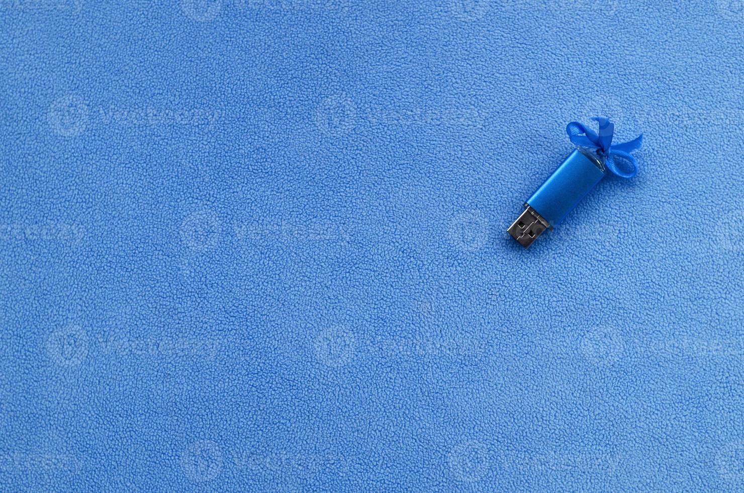 Brilliant blue usb flash memory card with a blue bow lies on a blanket of soft and furry light blue fleece fabric. Classic female gift design for a memory card photo