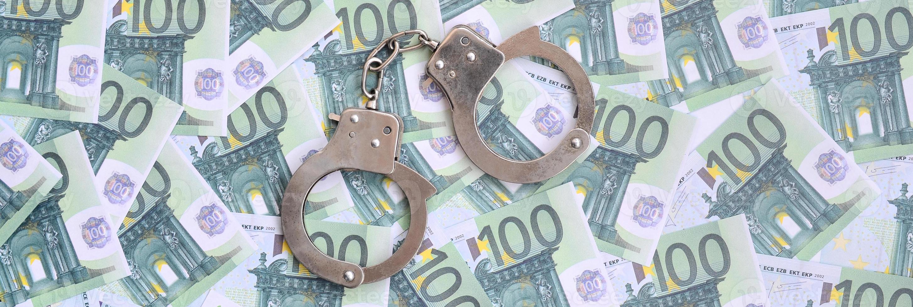 Police handcuffs lies on a set of green monetary denominations of 100 euros. A lot of money forms an infinite heap photo