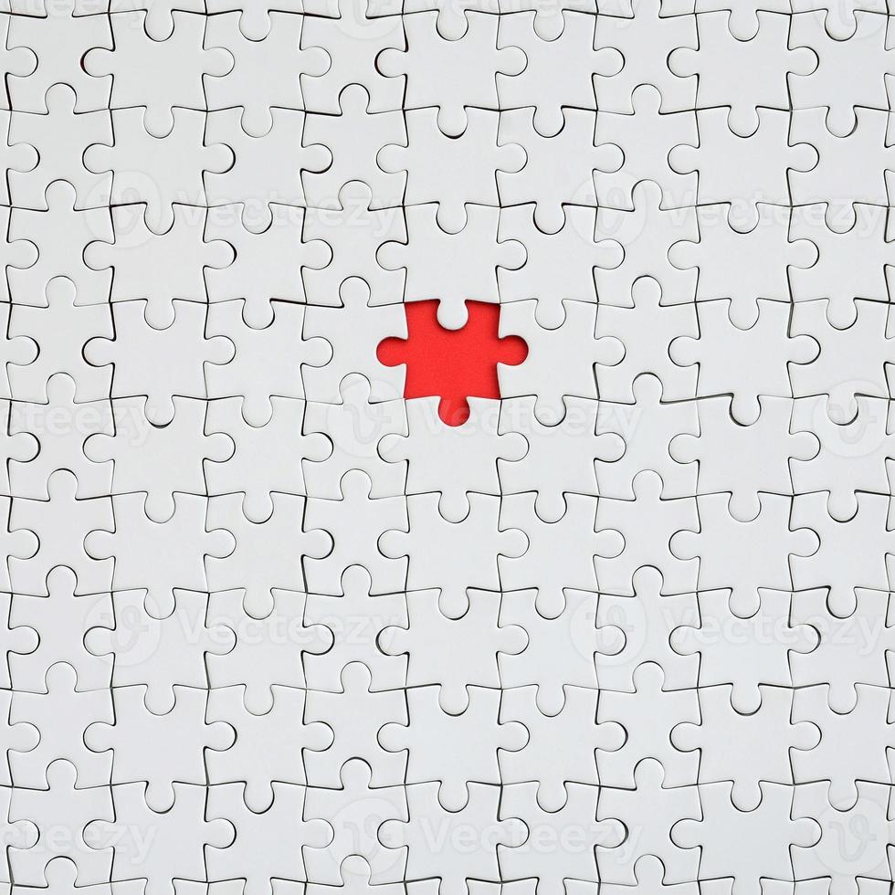 The texture of a white jigsaw puzzle in an assembled state with one missing element forming a red space photo