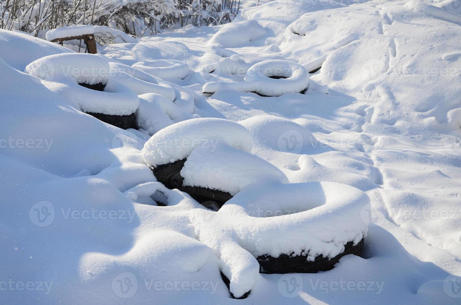 Used and discarded car tires lie on the side of the road, covered with a thick layer of snow photo